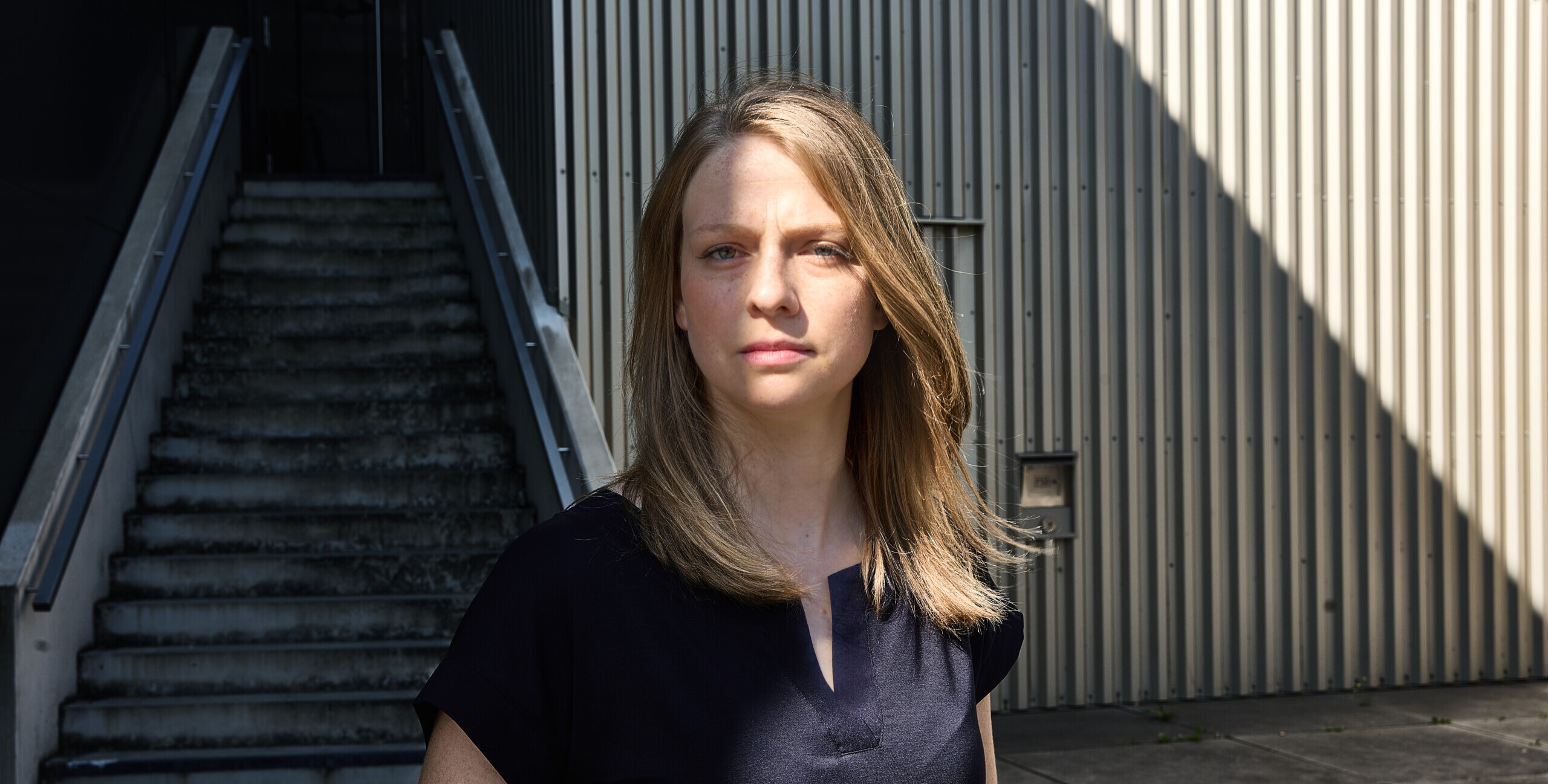 Das Portrait zeigt Sylvie Hahn, eine blonde Frau, im Halbschatten. Sie blickt ernst in die Kamera.