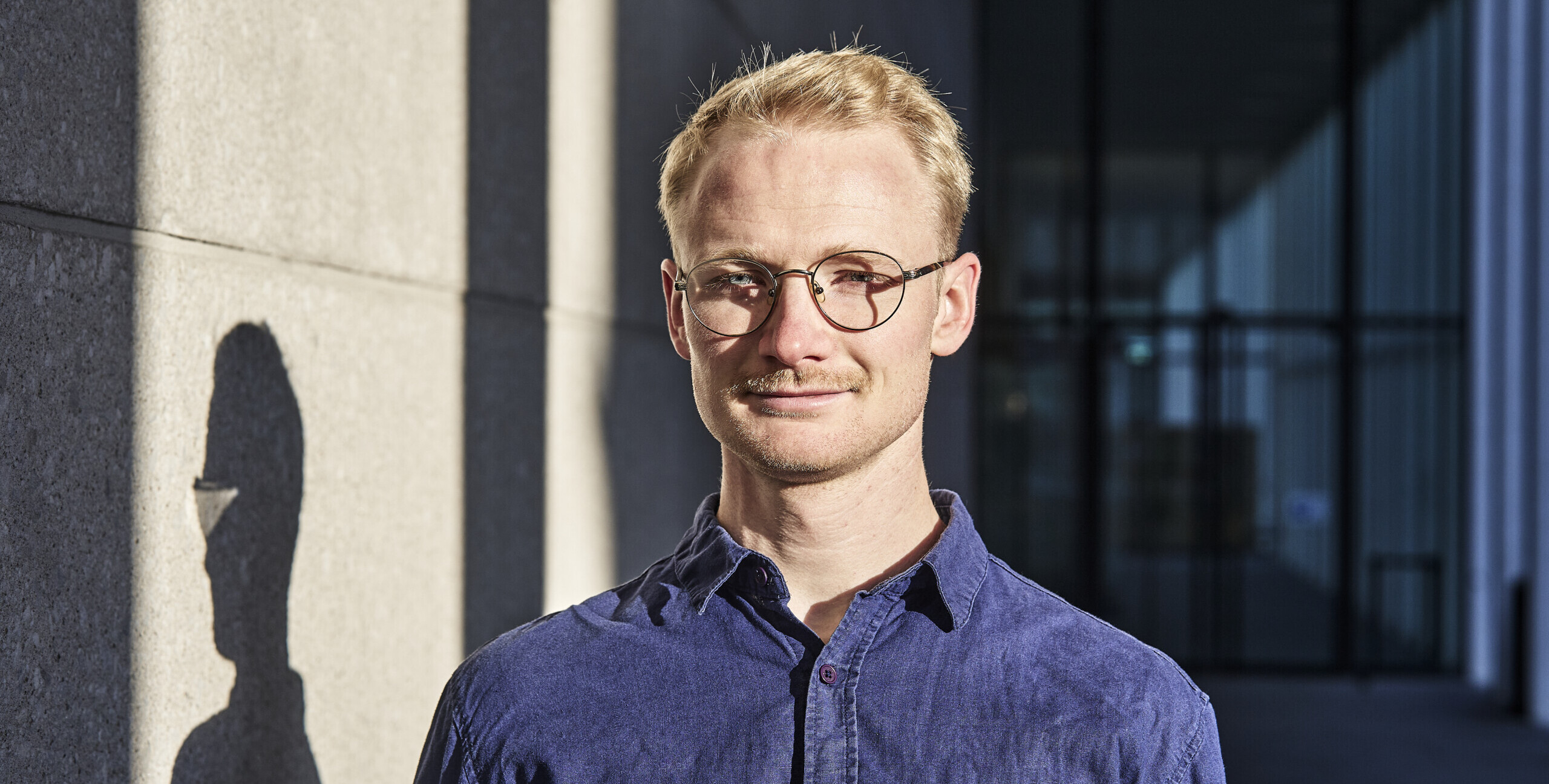 Das Portrait zeigt Fiete Lembeck, einen blonden Mann im Halbschatten. Er lächtelt in die Kamera.